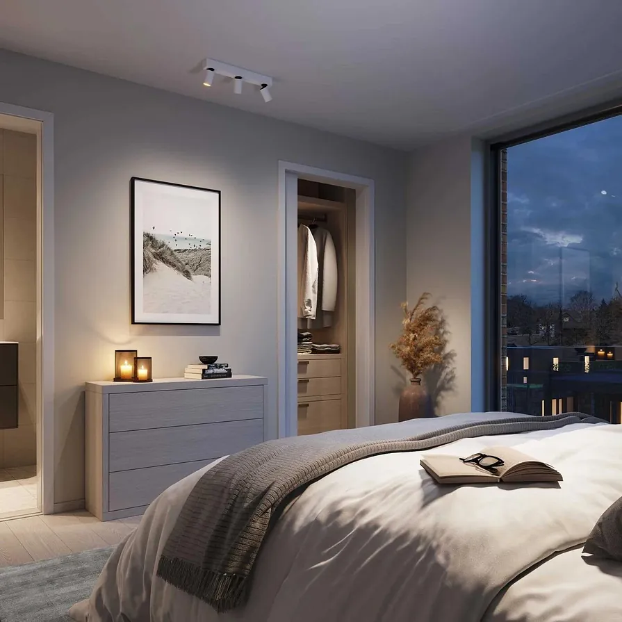 Soverom i varme toner med åpen dør til bad og walk-in, og store vinduer mot kveldshimmel.