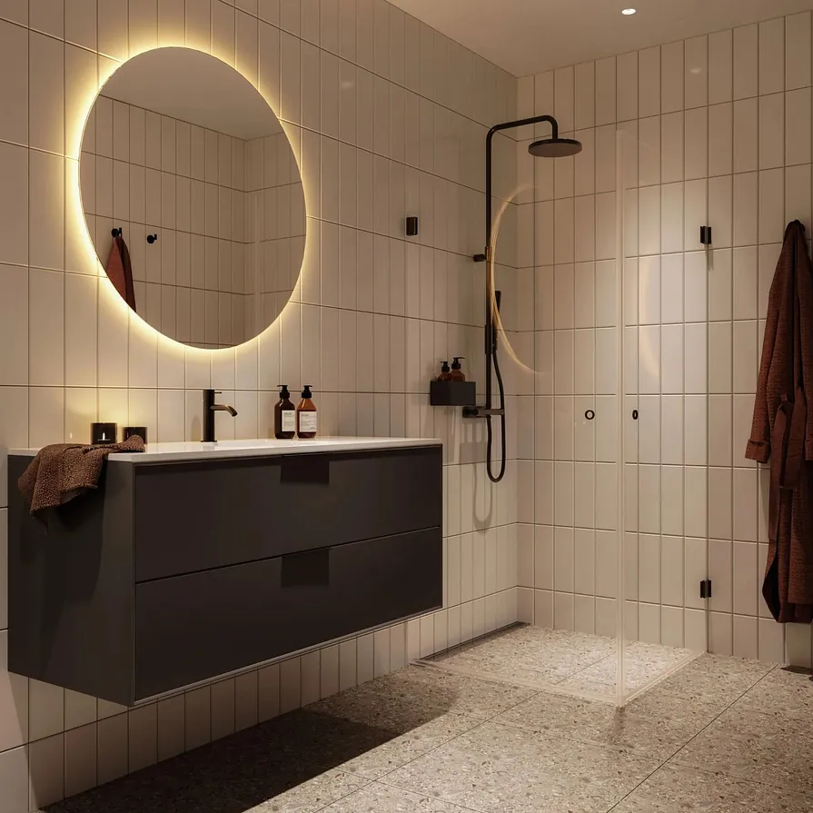 Bad med store fliser, rund bakbelyst speil, mørk servant og dusj med sorte detaljer.